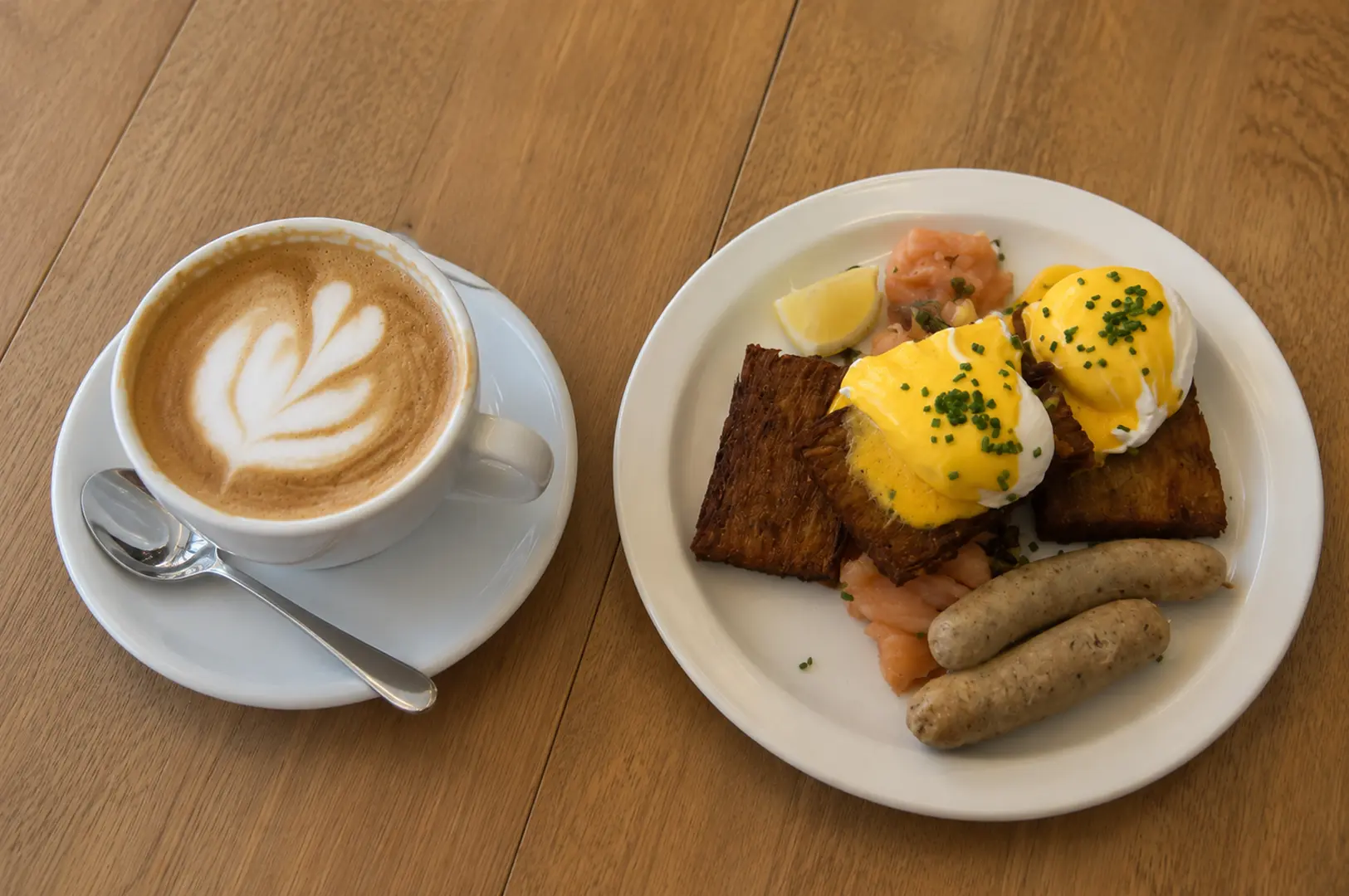 Eggs Benedict with smoked salmon, sausages, and a cup of latte for a hearty breakfast.