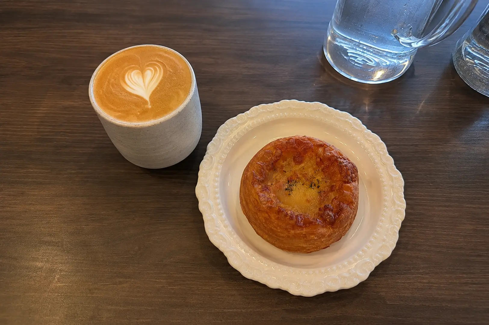 Hot latte served with a flaky cheese pastry on a decorative white plate.
