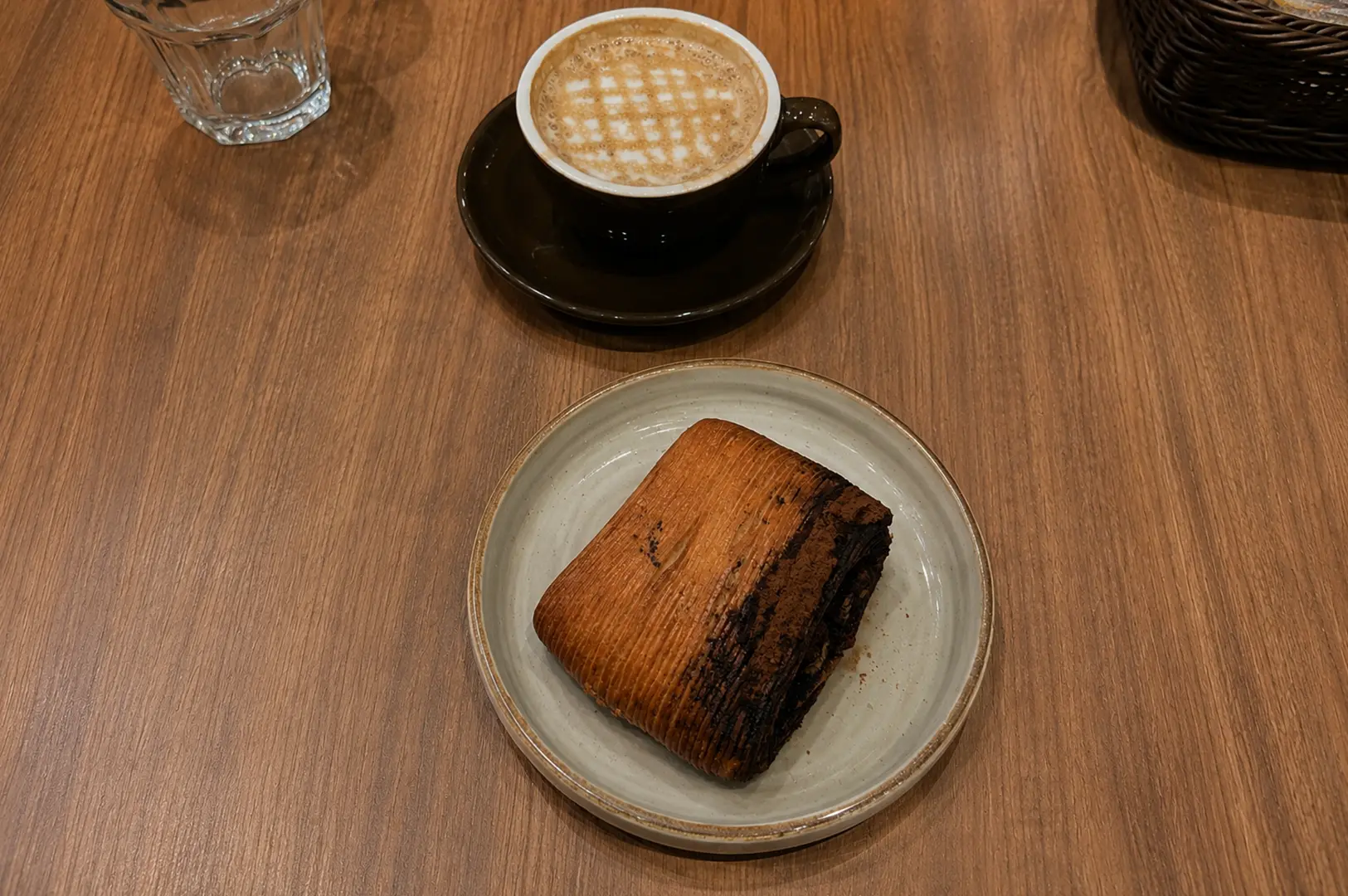 Cappuccino with foam pattern paired with a rich chocolate pastry on a ceramic plate.