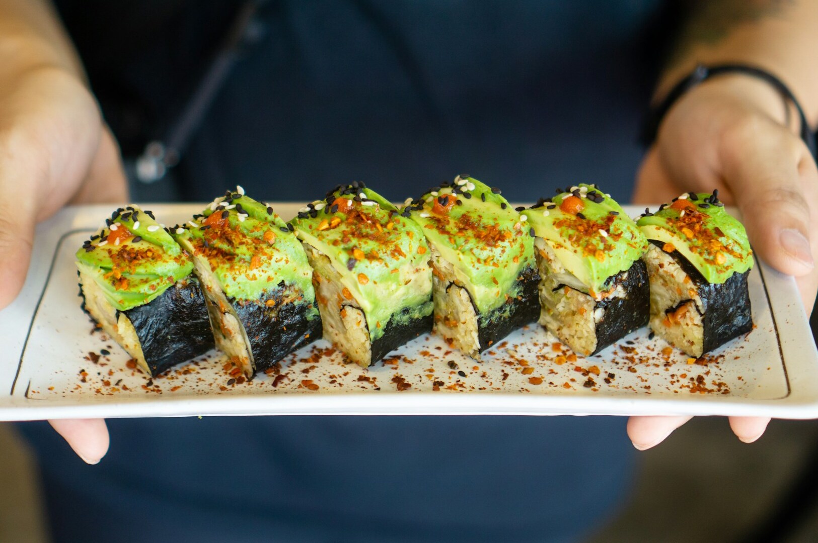 A person holding a plate of vegan sushi, showcasing a colorful assortment of plant-based ingredients in Singapore.