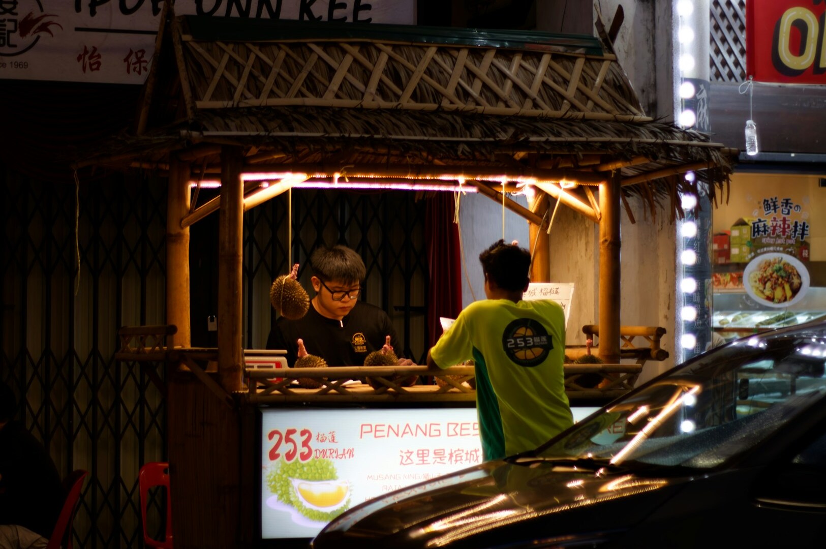A man stands by a food stand, representing the rich culinary exploration found at Hawker Stalls in Food Street.