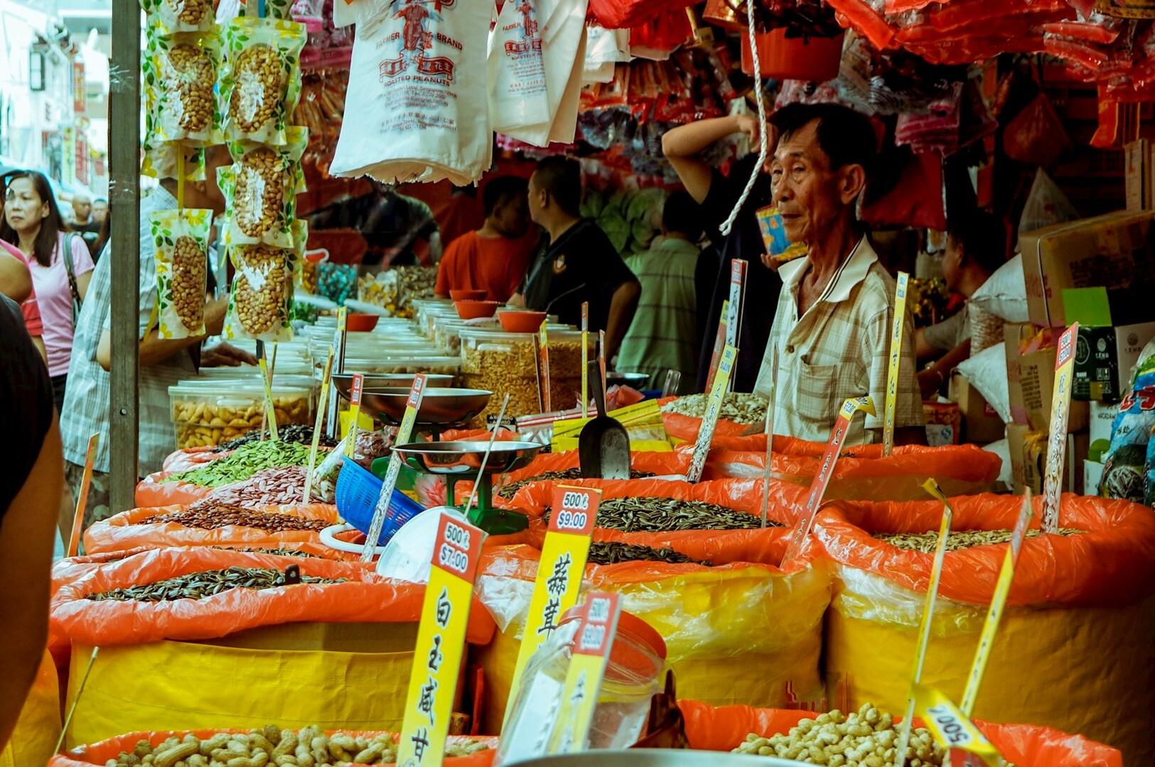 A man stands in front of a vibrant market filled with various food items, showcasing the lively atmosphere of Chinatown Street Market.