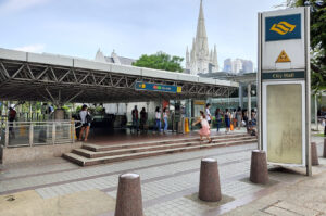 A bus stop near City Hall MRT Station in Singapore, with pedestrians walking by on a busy urban street.