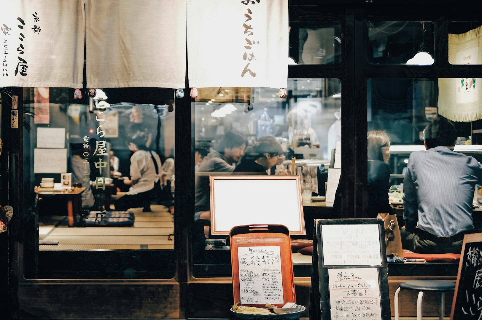 Interior of a Japanese Izakaya featuring patrons at tables and a prominent sign displayed on the wall.