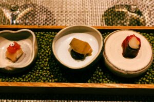 A wooden tray holds three small dishes, highlighting the exquisite flavors of Omakase cuisine in Singapore.