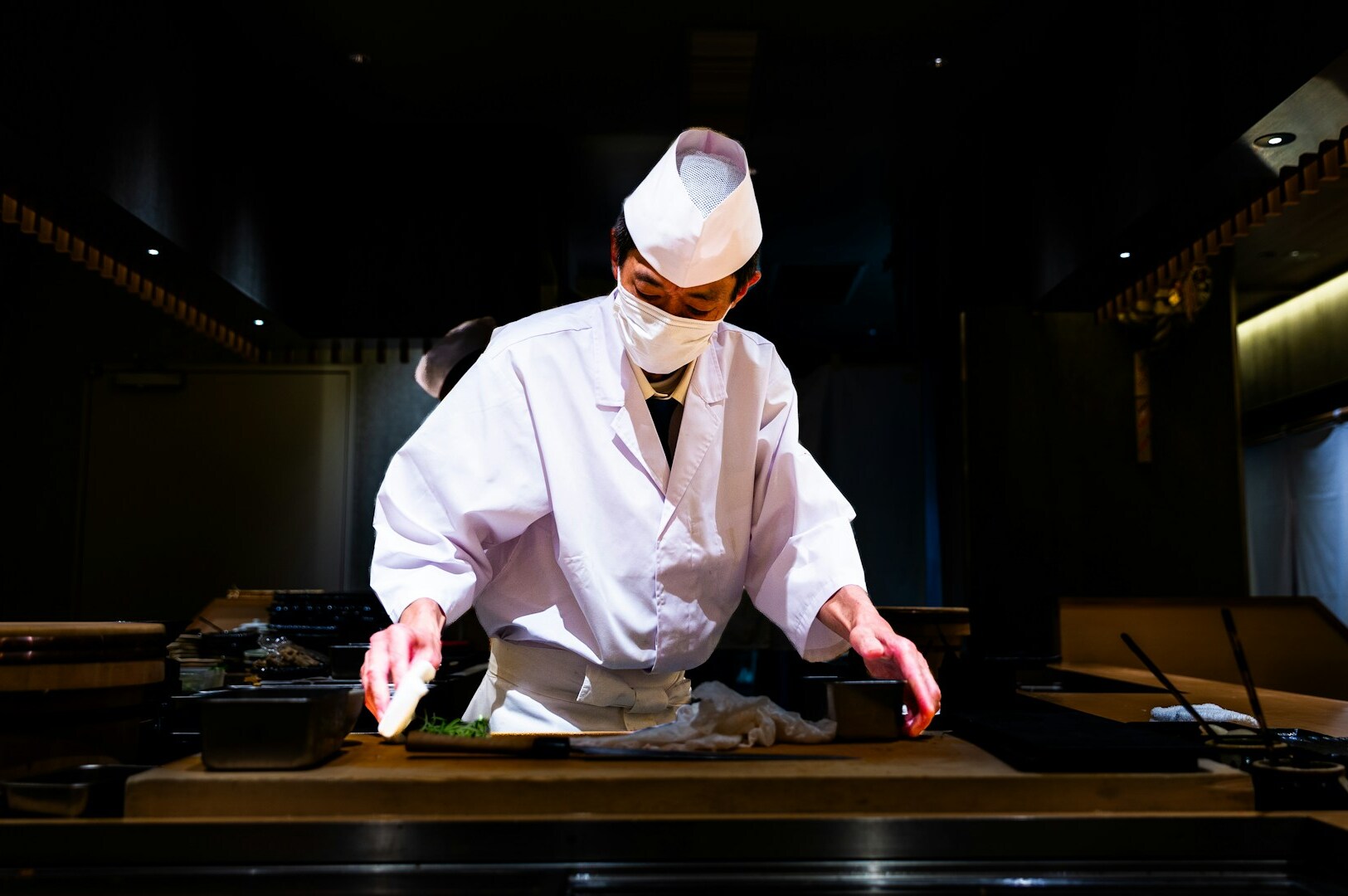 A man in a white coat meticulously prepares sushi, highlighting the omakase dining experience in Singapore.