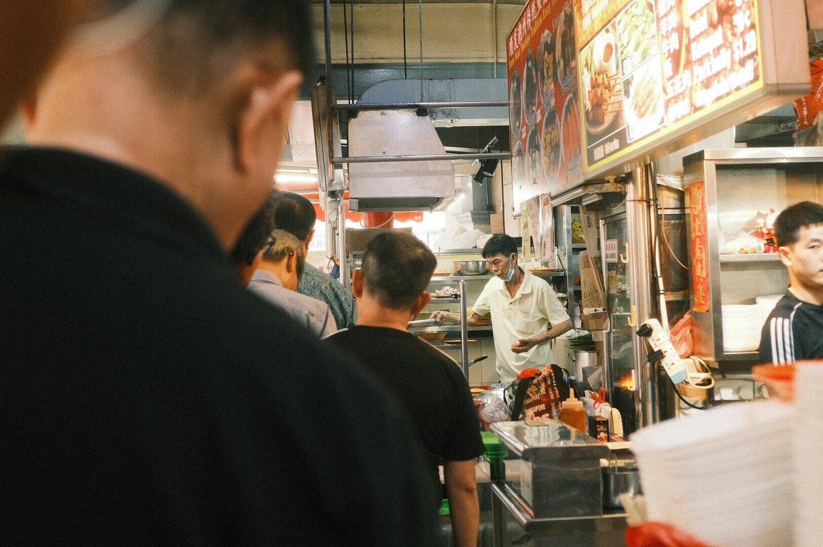 People standing in front of a vibrant hawker food stand in Singapore, showcasing various local dishes.