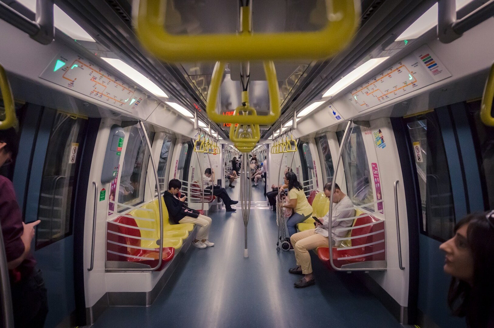 Passengers sitting on the seats of a Singapore MRT subway train, some reading and others using their phones.