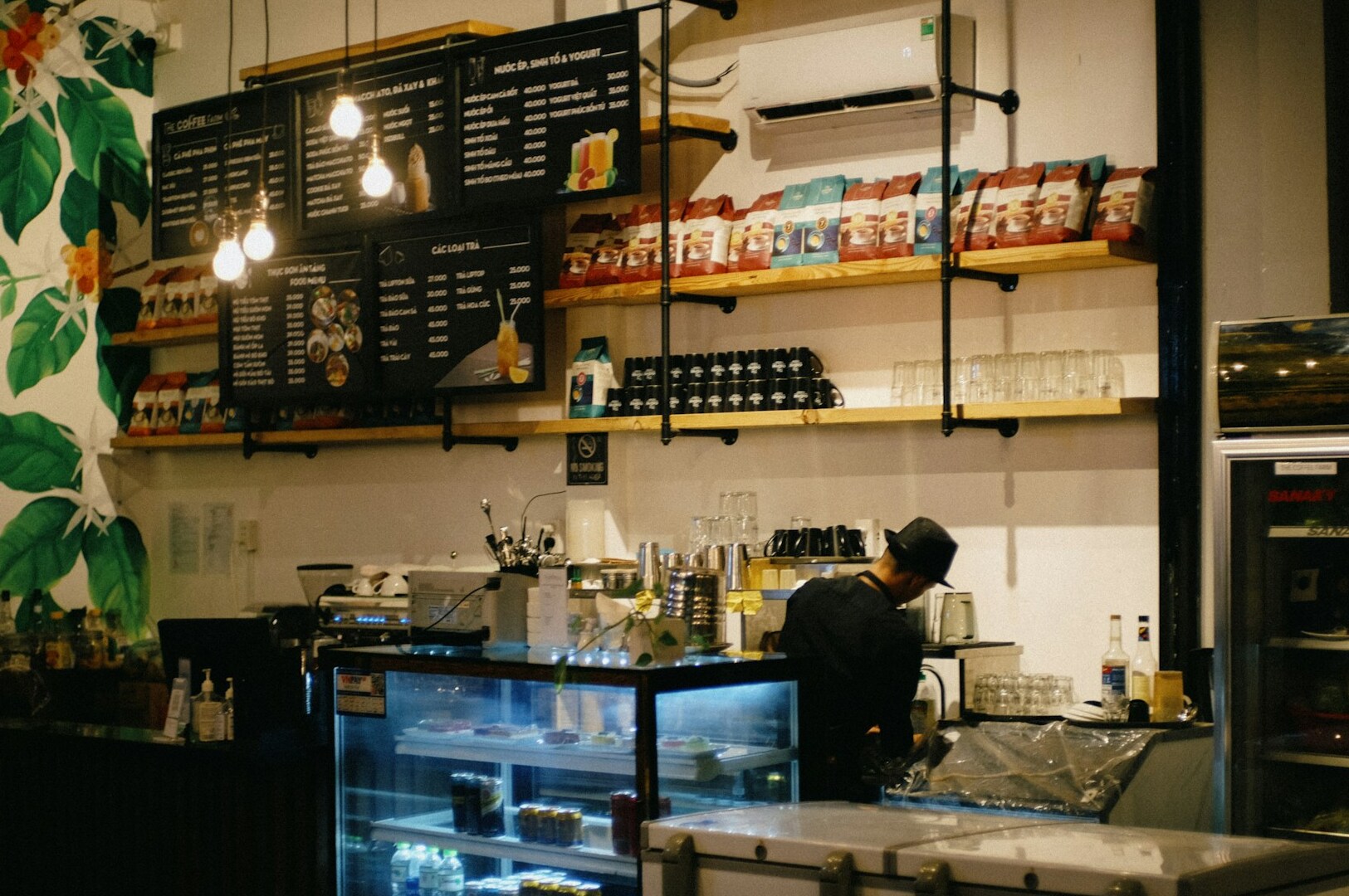 A man stands behind the counter at a coffee shop, ready to serve customers in a cozy, quiet atmosphere.
