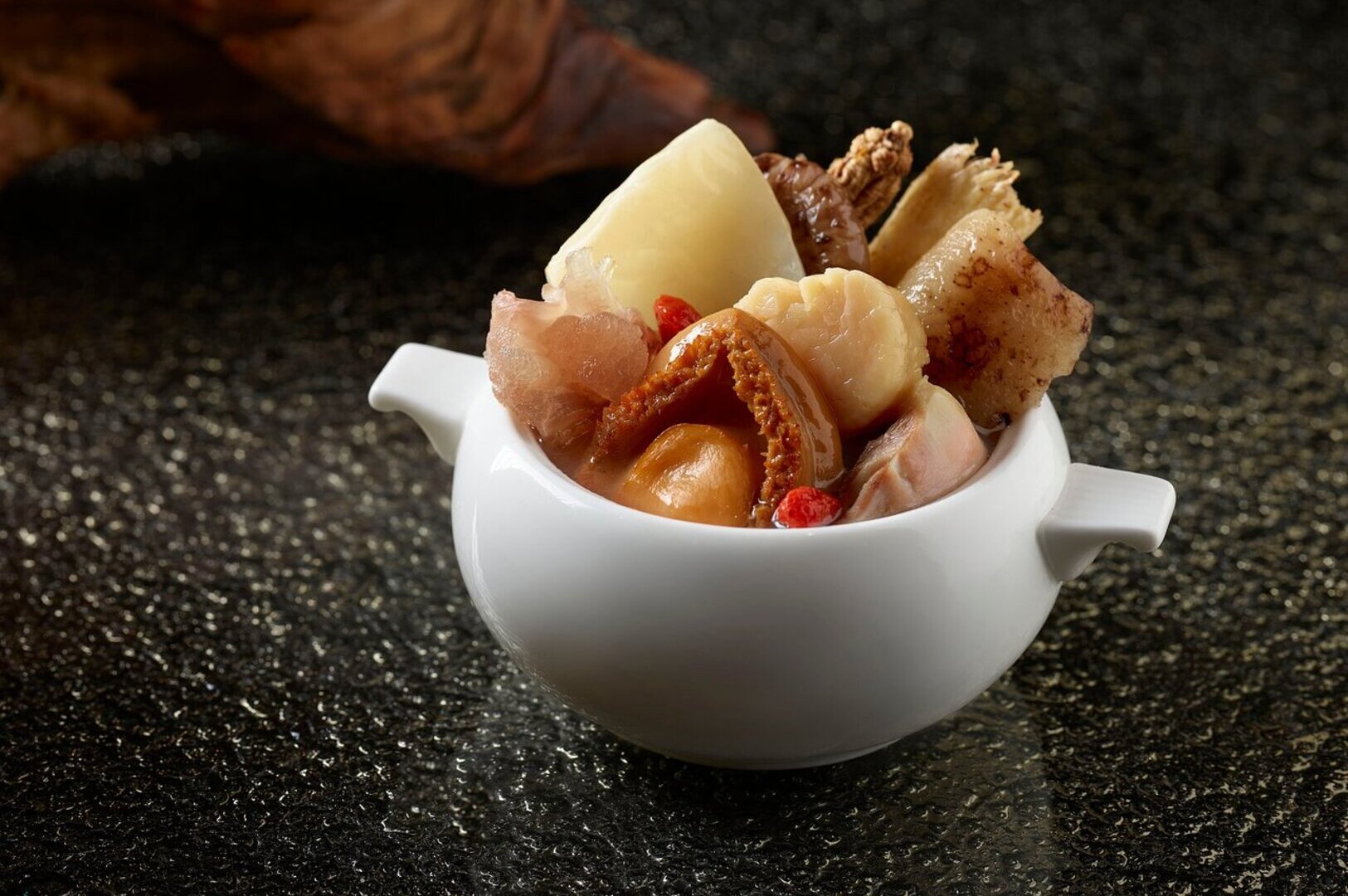 A bowl of Buddha Jump Over the Wall dish on a black surface, showcasing a rich and colorful assortment of ingredients.