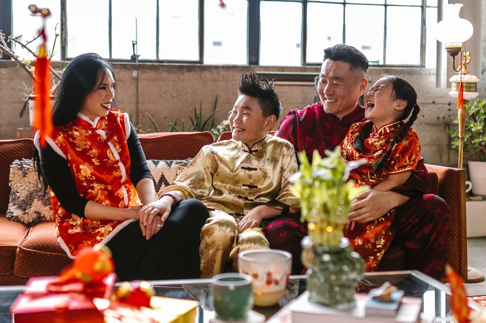 A family of four dressed in traditional Chinese clothing, celebrating Chinese New Year 2026, sitting together on a couch.