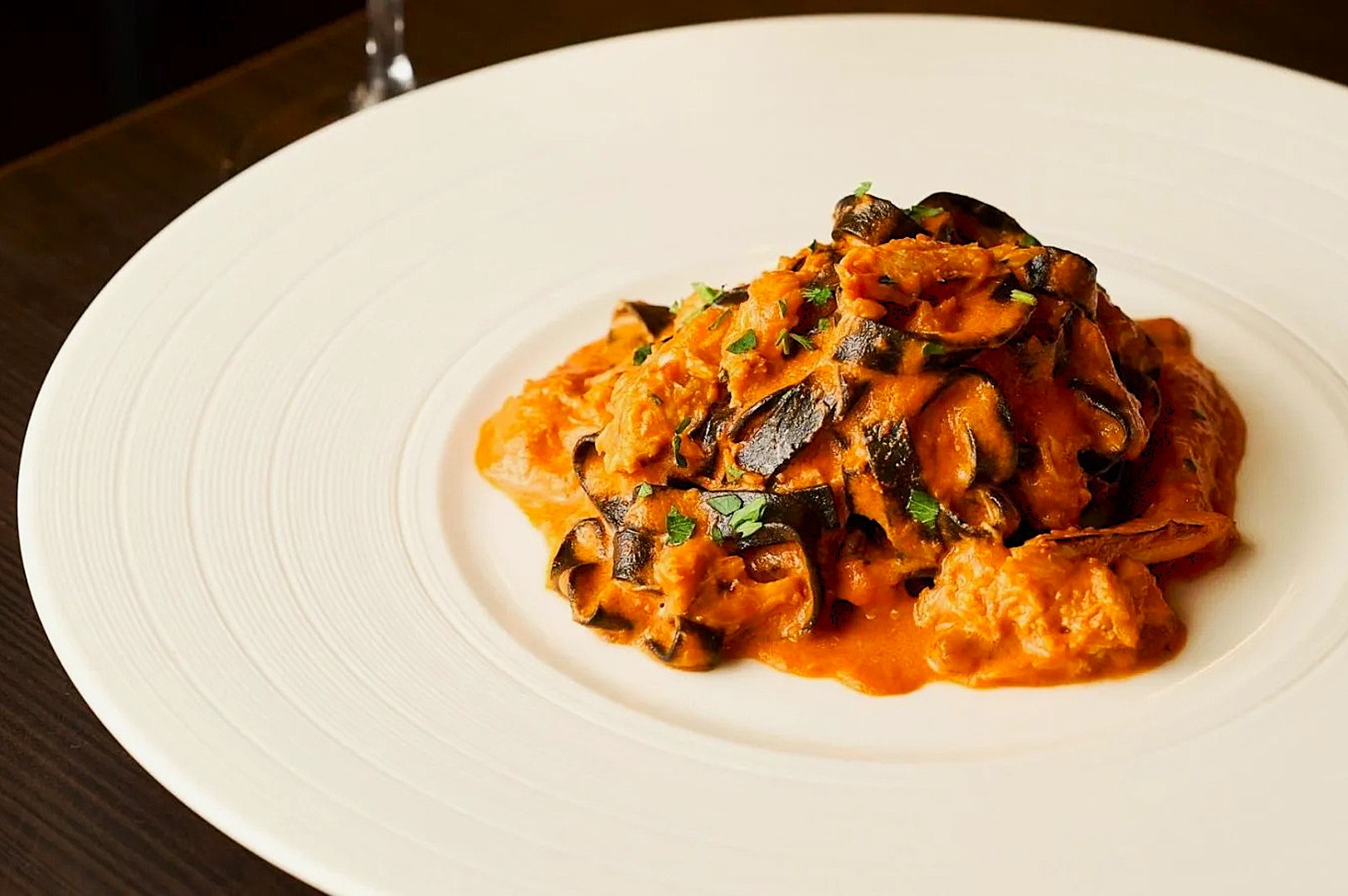 A gourmet dish featuring black and white striped pasta in a rich orange sauce, garnished with herbs, elegantly presented on a white plate.