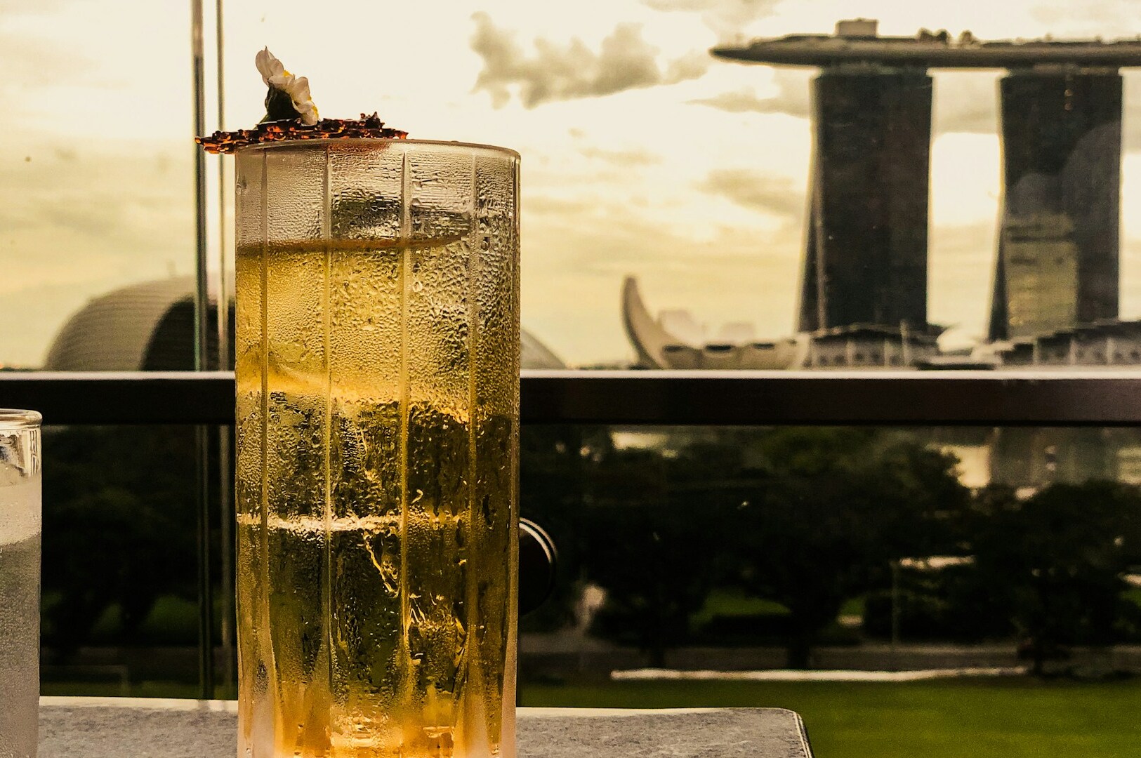 A cocktail on a table with a panoramic view of Singapore's skyline featuring Marina Bay sands in the background.