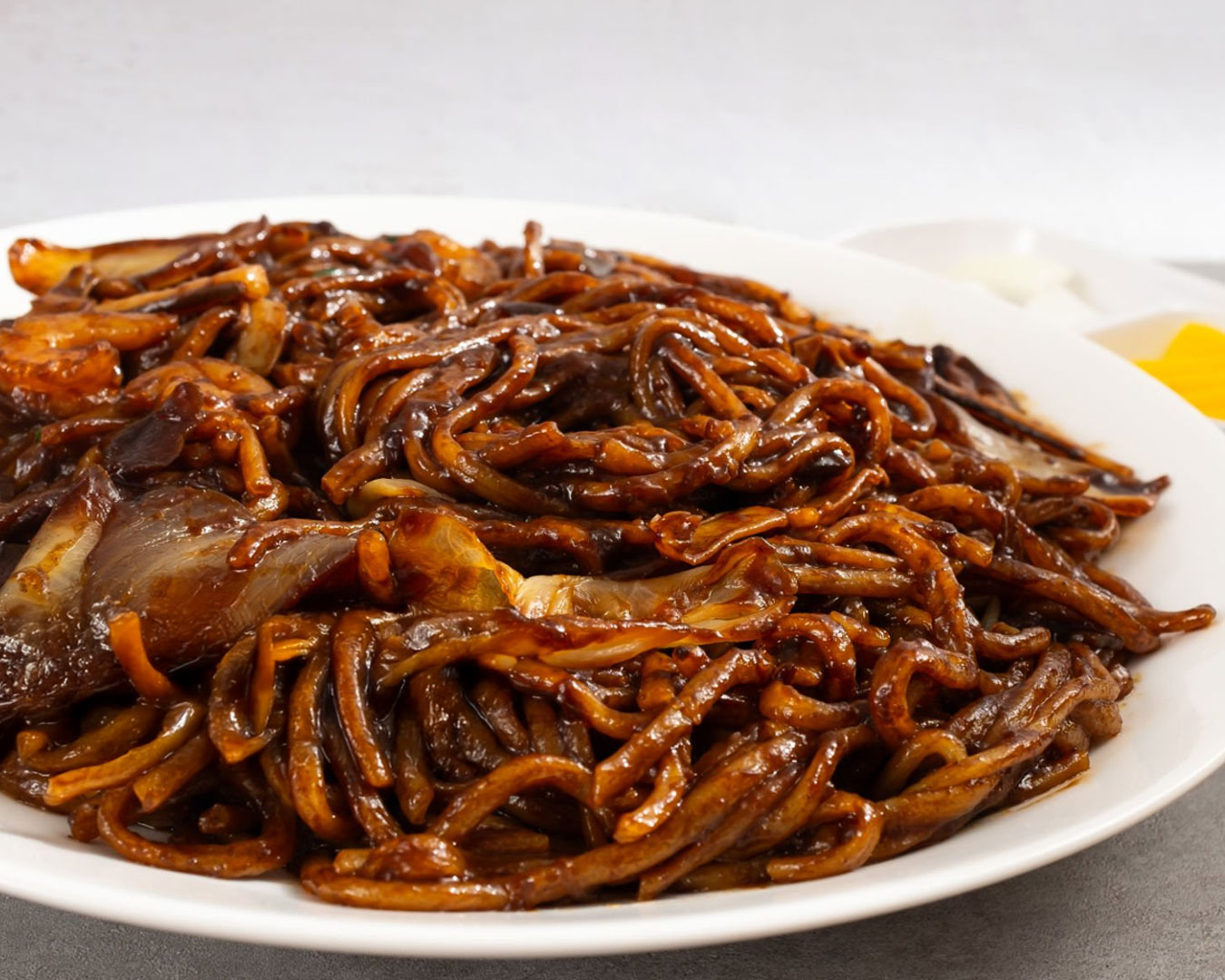 A plate of thick yellow and rice noodles cooked in dark savoury sauce with prawns and pork slices, topped with crispy lard and lime on the side.