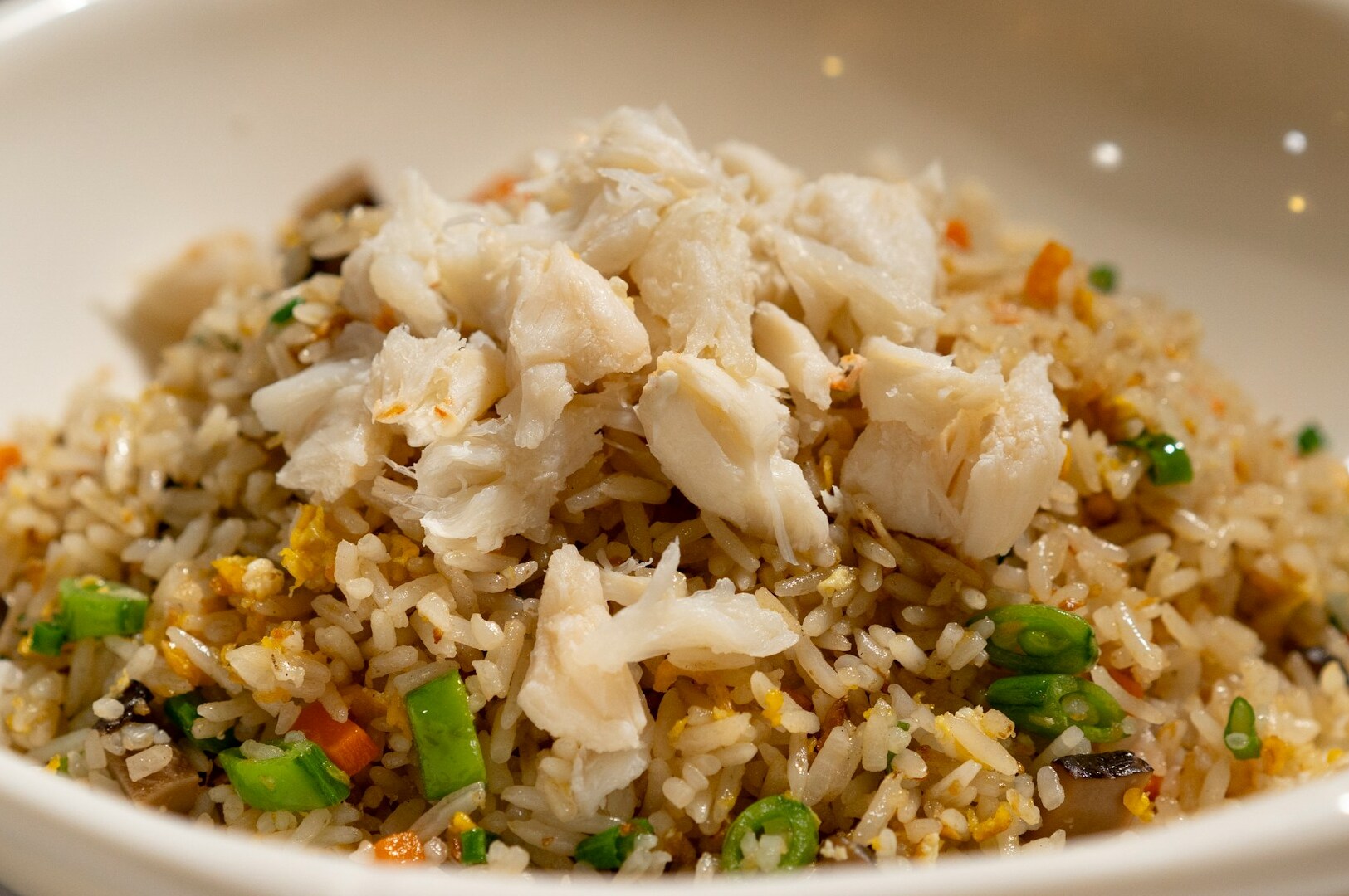 A close-up of a plate of crab fried rice topped with chunks of crab meat, colorful vegetables, and green onions. The dish looks appetizing and savory.