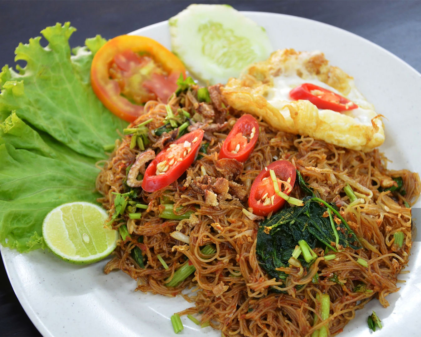 A plate of golden-brown fried noodles mixed with vegetables, egg, and light seasoning, giving a smoky wok-fried appearance.