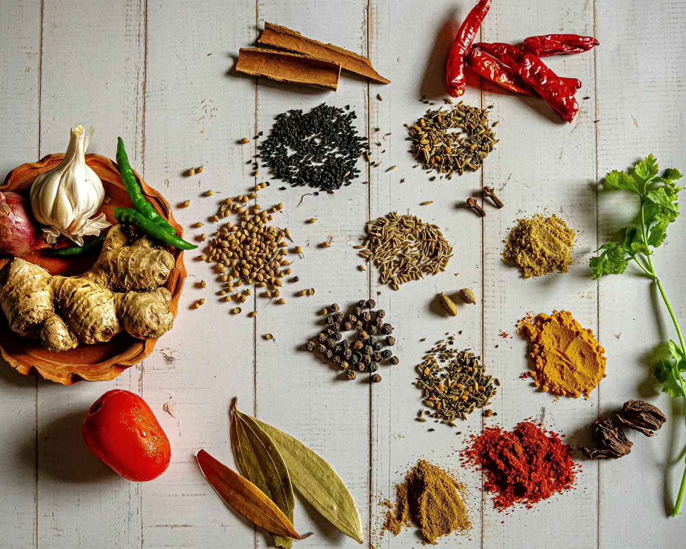 A close-up of assorted Indian spices including cumin seeds, black mustard seeds, and vibrant turmeric powder showcasing rich colours and aromatic ingredients commonly used in traditional cooking.