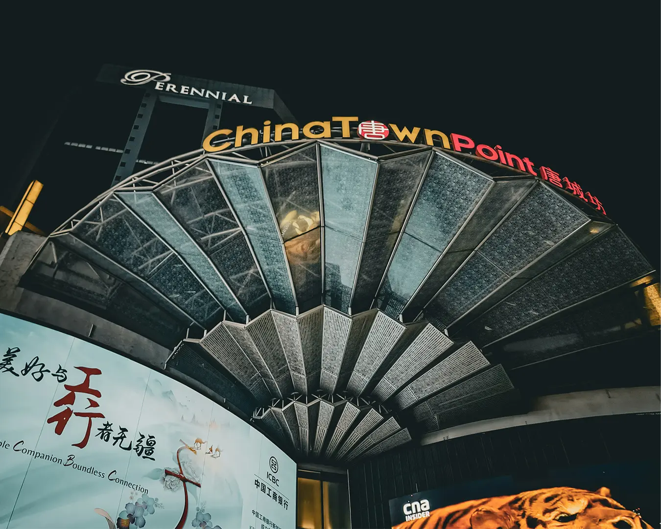 Brightly illuminated Chinatown signage mounted on a traditional-style building at night, glowing against the dark sky and city lights.