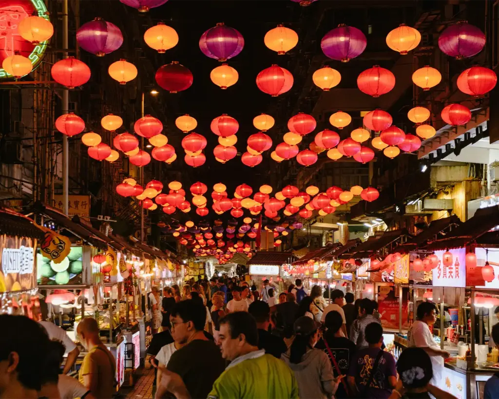 Crowds of people walking through a busy Chinatown street market, exploring food stalls and looking for local street food at night.