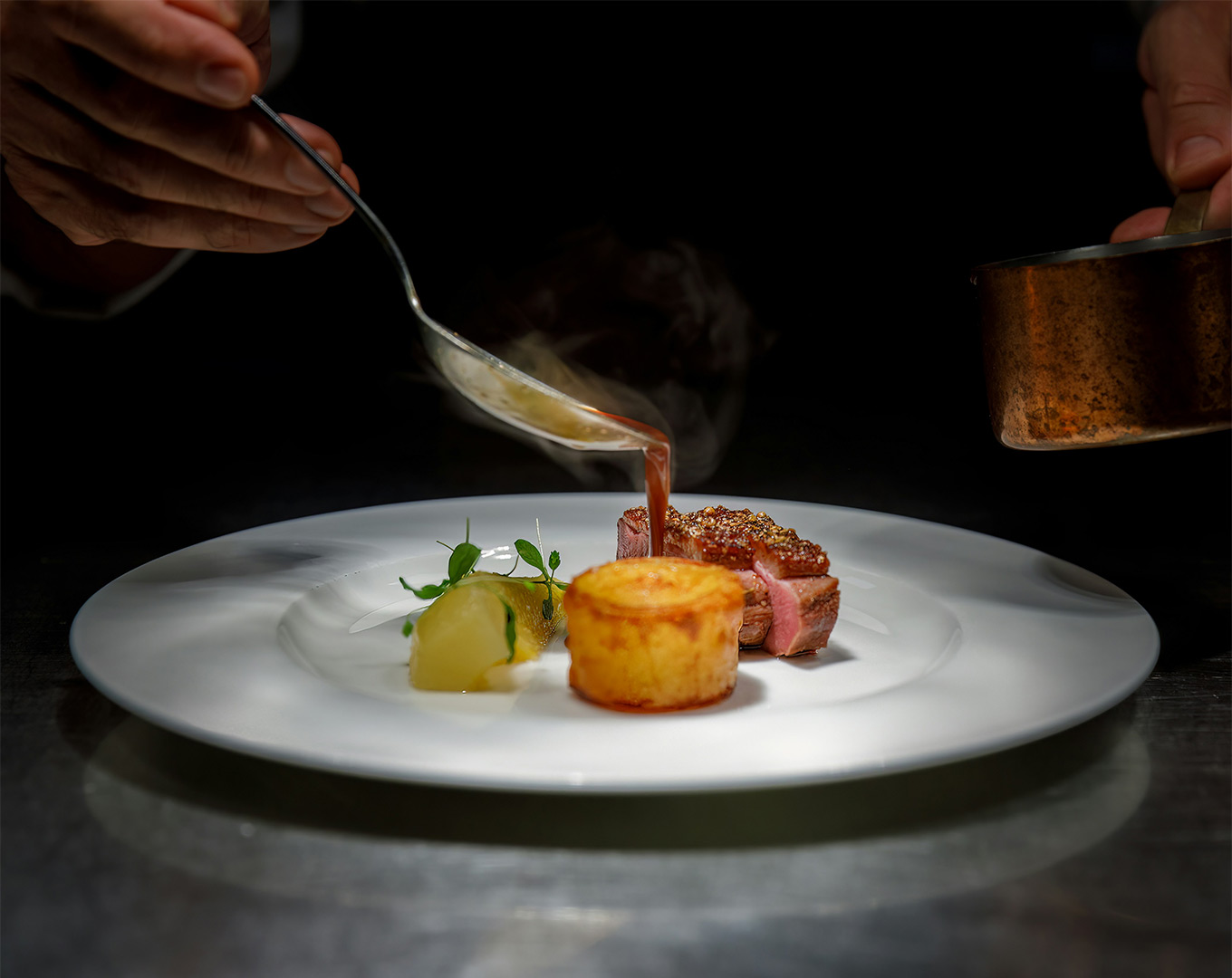 A chef carefully pours a glossy sauce over a plated dish, creating a flowing motion that enhances the visual richness and final refinement of the cuisine.