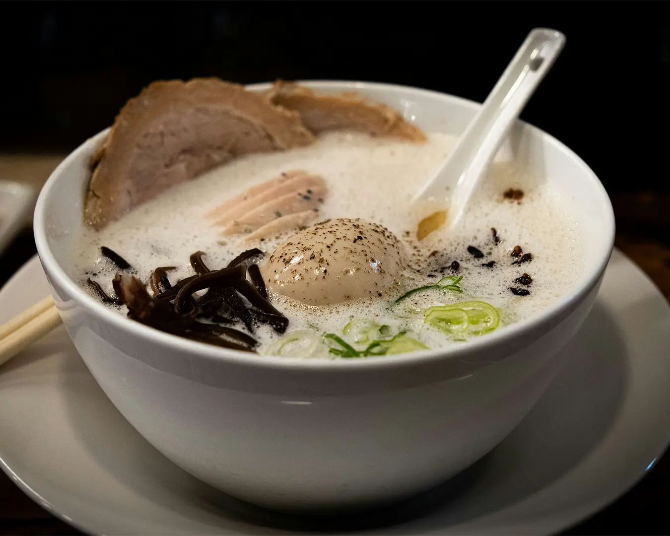 A steaming bowl of ramen topped with sliced meat, soft-boiled egg, and fresh garnishes, capturing the comforting and rich flavours of Japanese noodle soup.