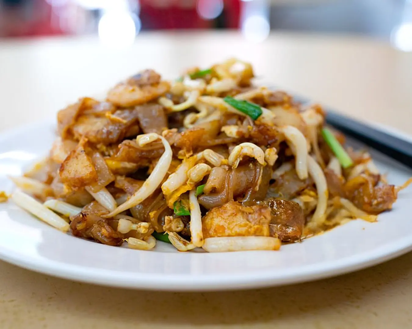 A freshly cooked plate of char kway teow, stir-fried flat rice noodles with prawns, egg, bean sprouts, and Chinese sausage, glistening from the wok’s smoky heat.