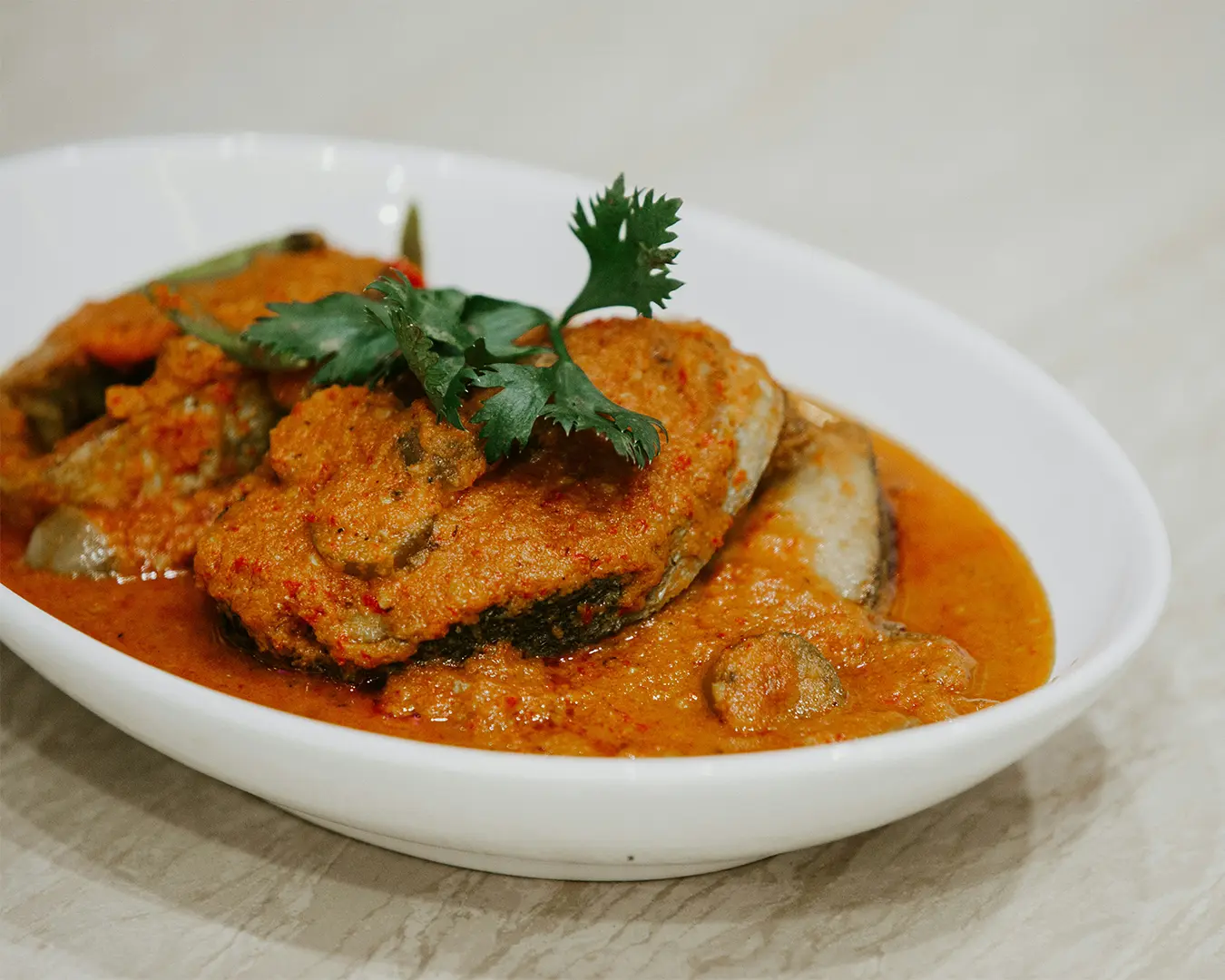 A vibrant fish head curry served in a deep dish, featuring tender fish immersed in a thick, spicy gravy with vegetables, reflecting a bold and iconic local delicacy.