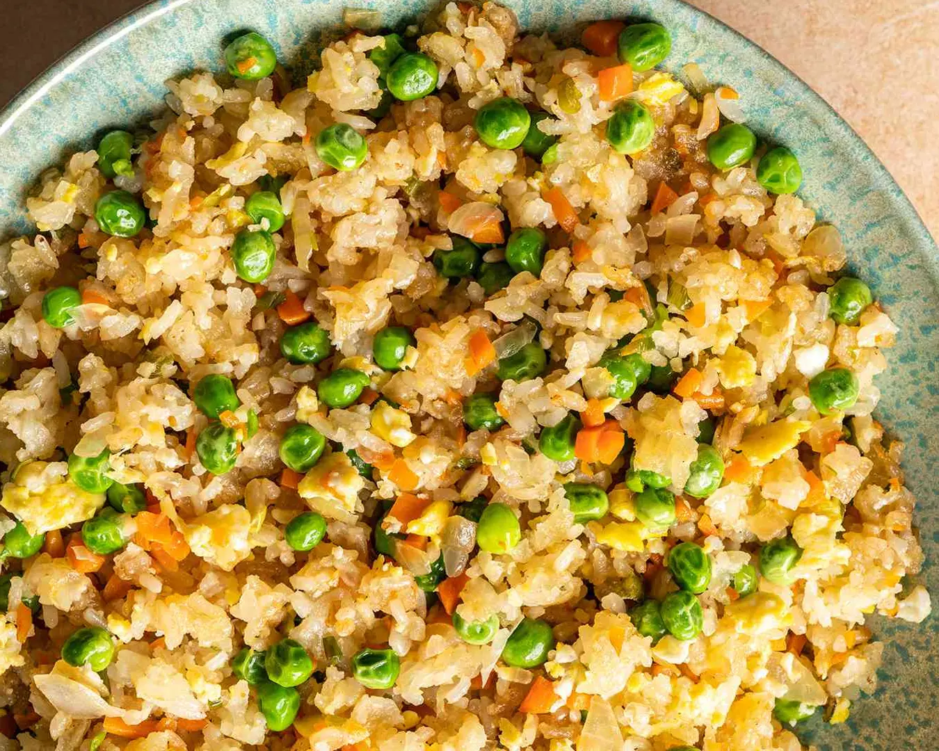 A plate of golden fried rice mixed with diced vegetables like carrots, peas, and corn, garnished with fresh herbs for added flavour.