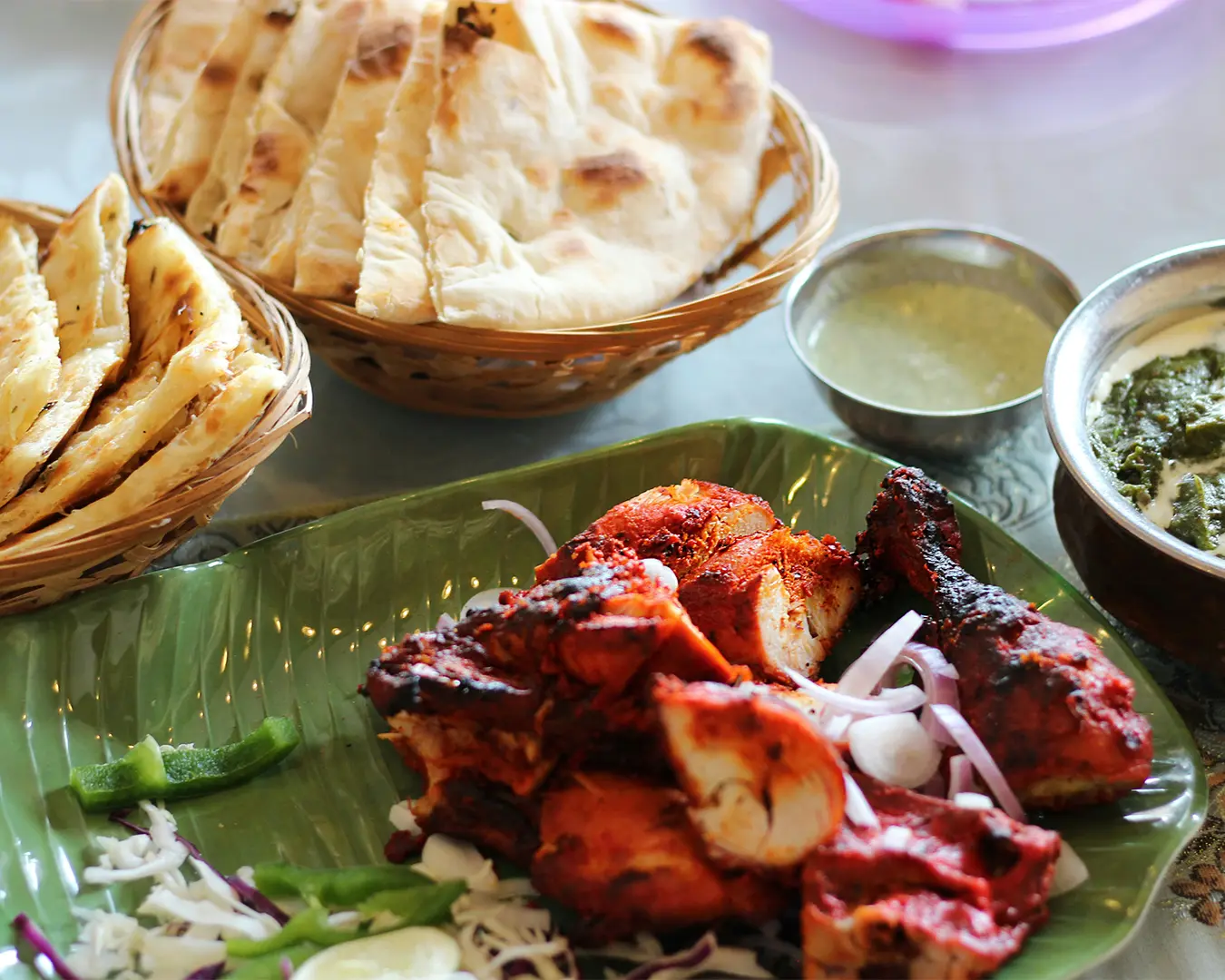 An assortment of tandoori dishes including grilled meats with a smoky char, coated in spiced marinade, presented on a platter that highlights bold colours and textures.