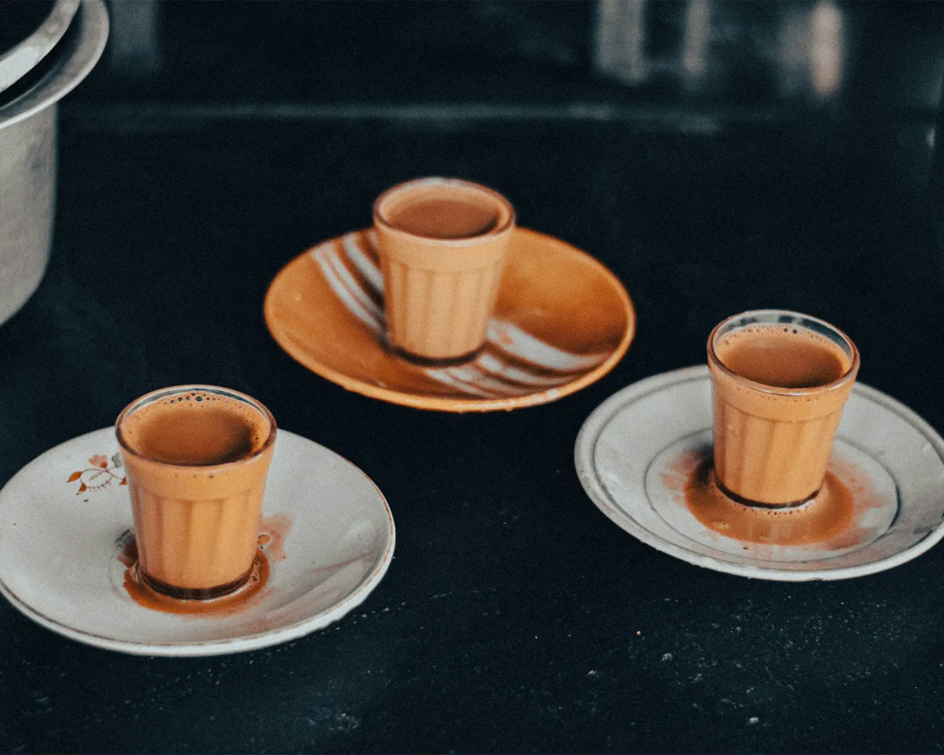 Three clear glasses filled with steaming masala chai, showing its warm brown tone and creamy texture, placed together to evoke a cosy and inviting tea moment.
