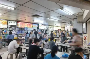 Busy hawker centre interior with diners at tables and multiple food stalls with menu boards
