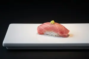 Single piece of tuna nigiri sushi with wasabi on white rectangular plate.