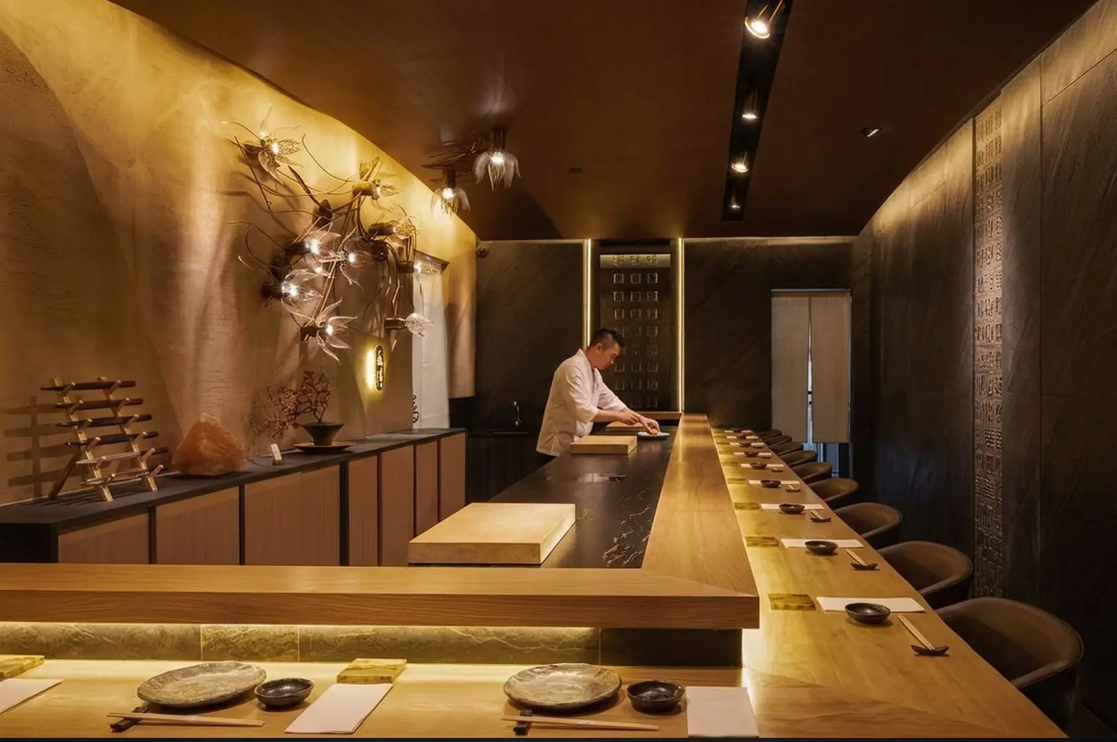 Elegant omakase dining counter with artistic branch lighting and chef preparing sushi