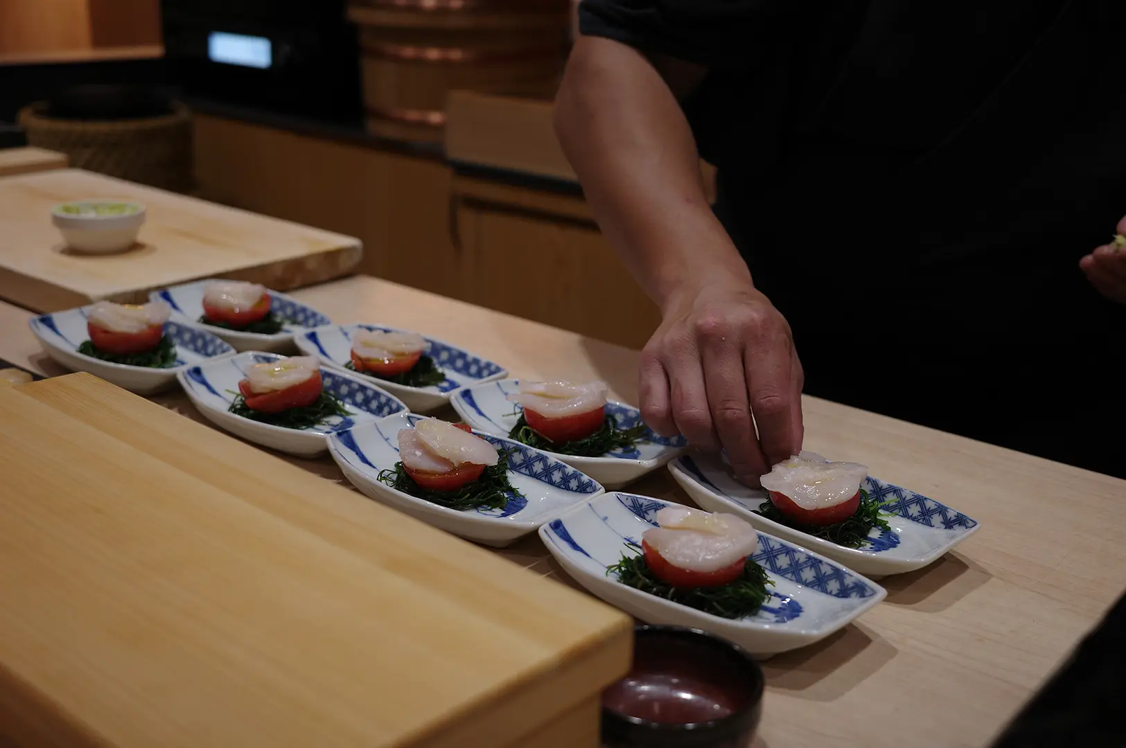 Sushi Sama chef arranging scallop sushi on individual Japanese plates at the counter, showing the preparation and presentation of the dishes.
