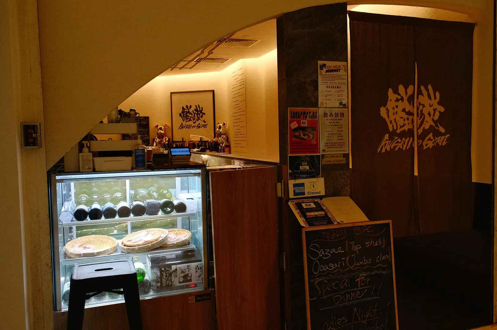 Sushi To Sumi entrance and reception area with a display case, Japanese artwork, and a warm, intimate restaurant setting.