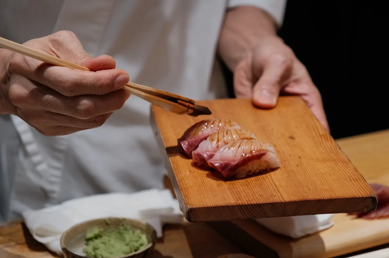 Chef serving freshly prepared nigiri on a wooden board, highlighting the hands-on sushi-making experience at Sushi To Sumi.