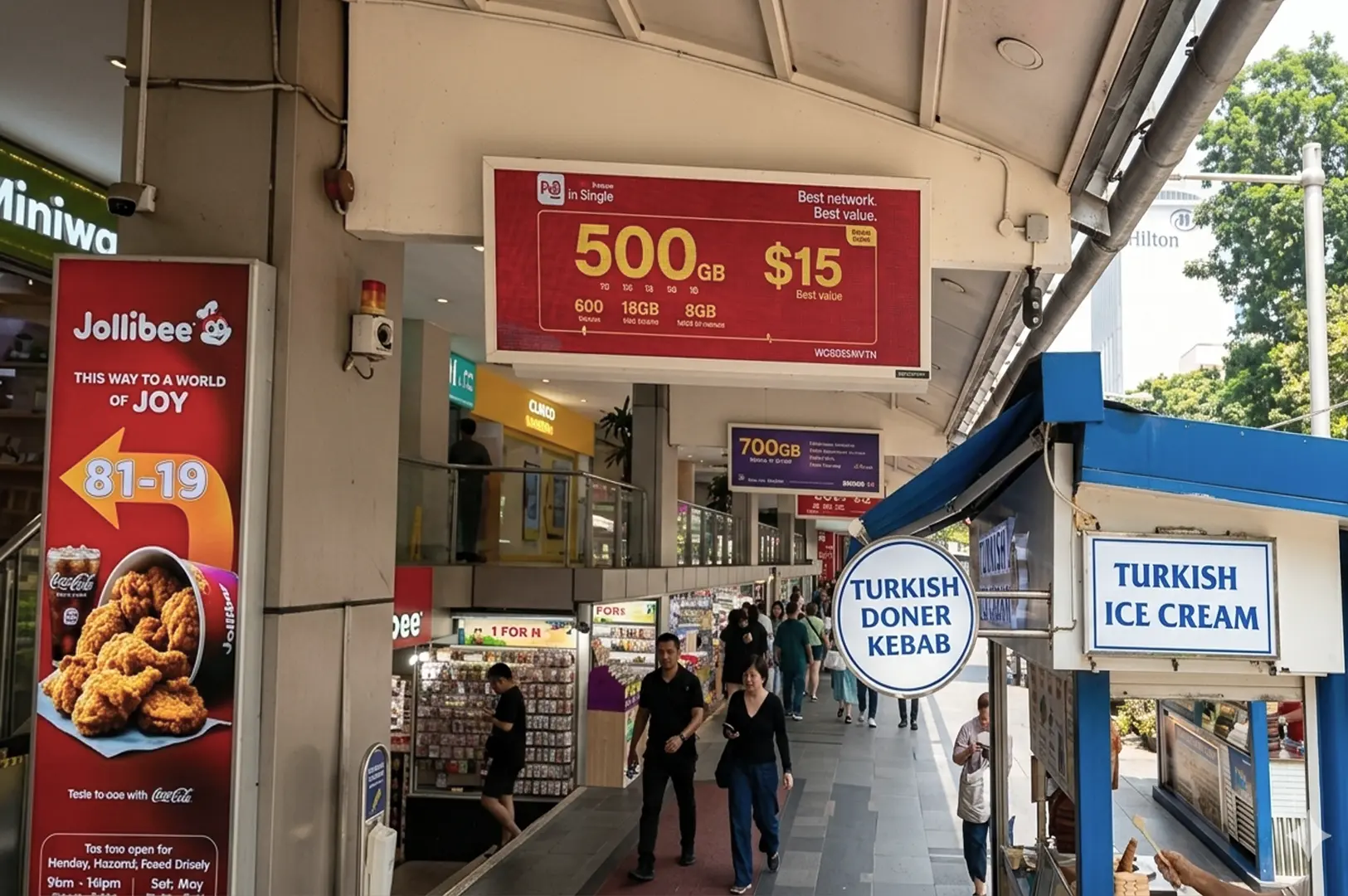 Covered walkway of food centre with Jollibee advertisement, Turkish kebab and ice cream stalls, and telecommunications signage