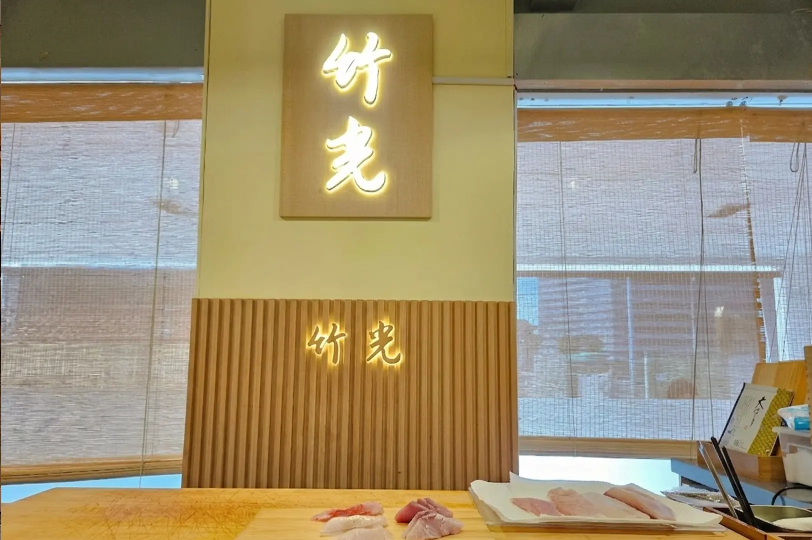 Takemitsu Omakase interior with illuminated kanji signage above bamboo paneling and fresh sushi at counter.