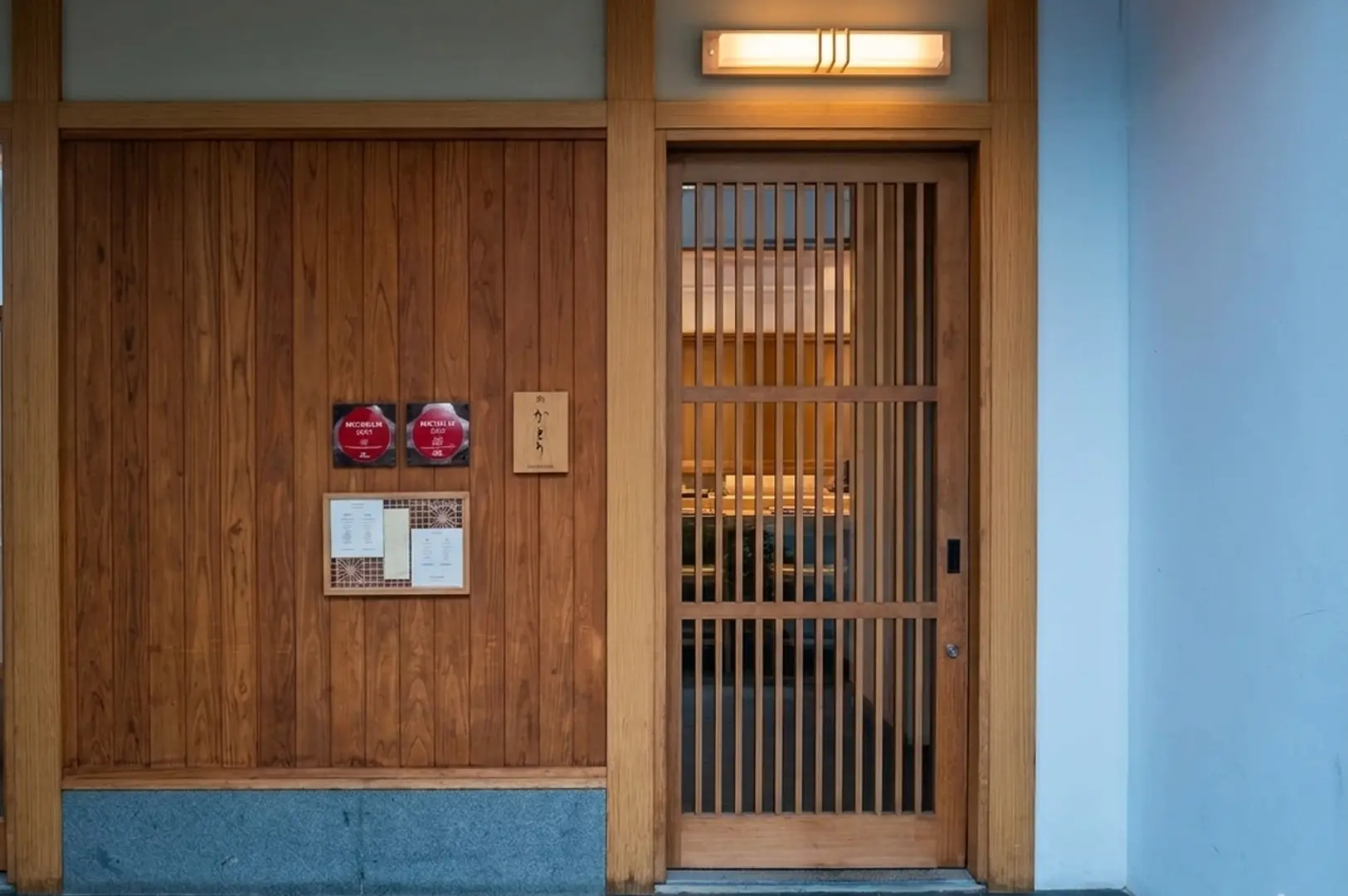 Wooden entrance of Sushi Katori with illuminated sign and Michelin guide plaques.