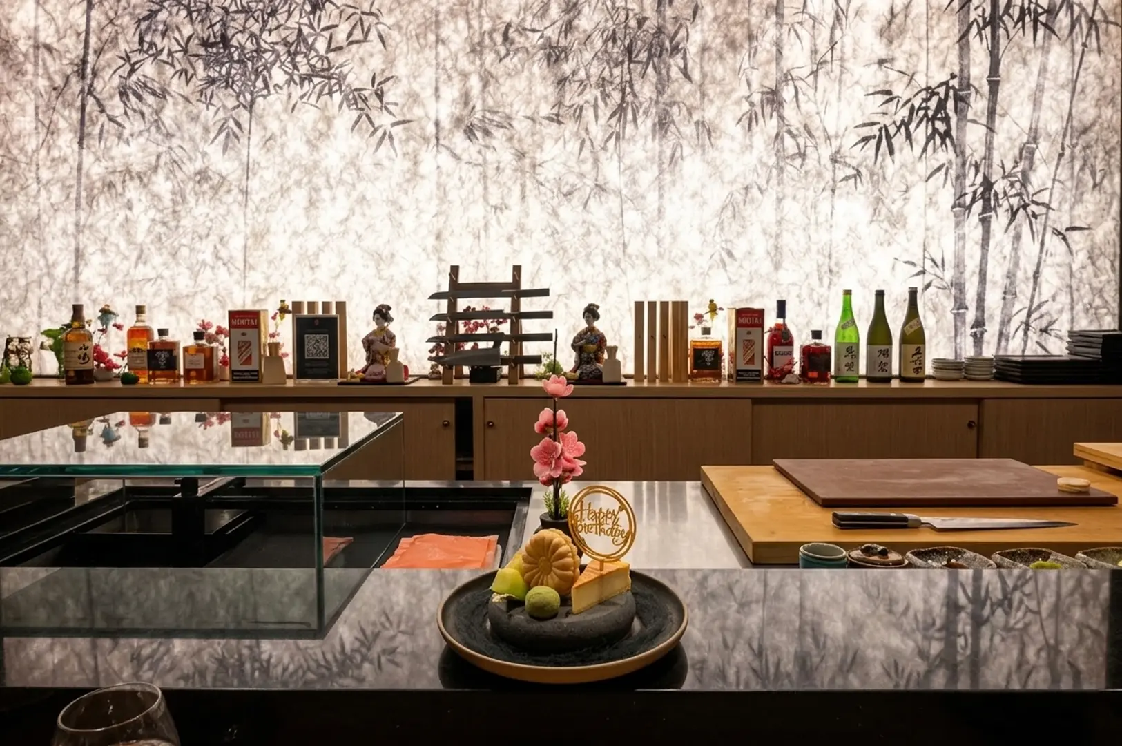 Honō Omakase sushi counter with bamboo forest backdrop, sake display, and birthday dessert plating.