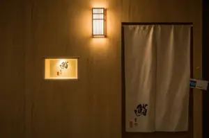 Entrance to the restaurant showing a white noren curtain with the calligraphy logo and an Open sign