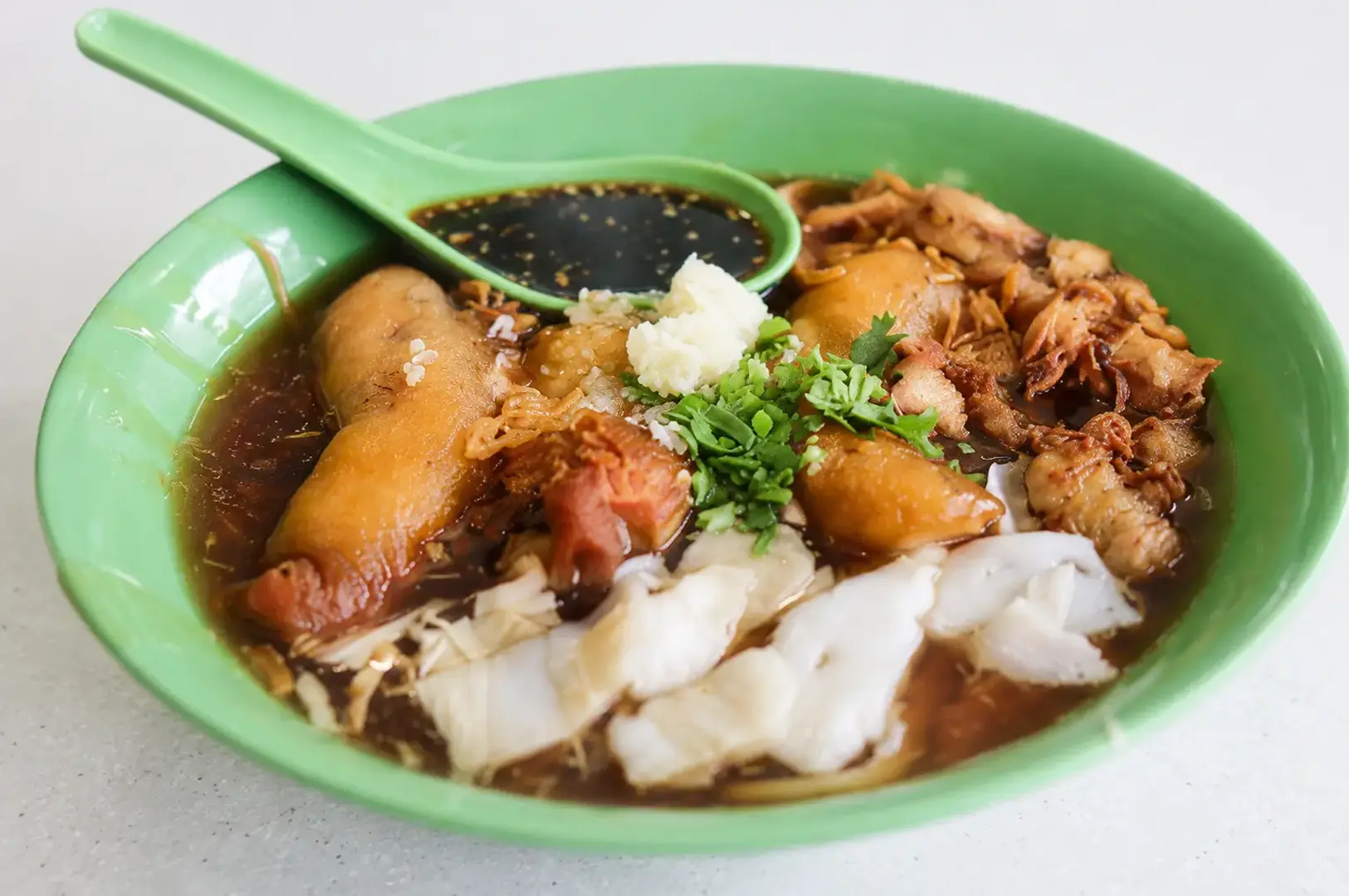 Green bowl of traditional herbal soup with meat, fish maw, and vegetables