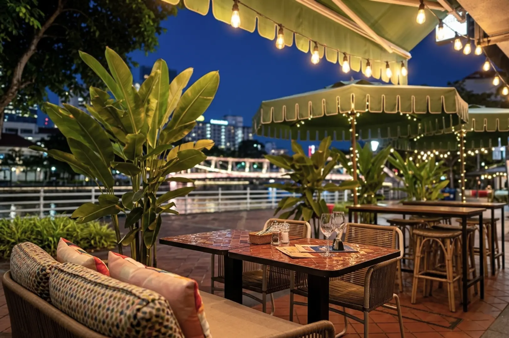 Cozy outdoor dining terrace at Robertson Quay with string lights and green awnings, offering scenic Singapore River views for a relaxed date night