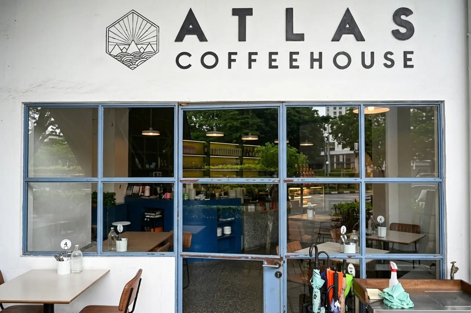 Exterior view of Atlas Coffeehouse storefront with white facade, blue-framed windows, and geometric mountain logo sign above the entrance