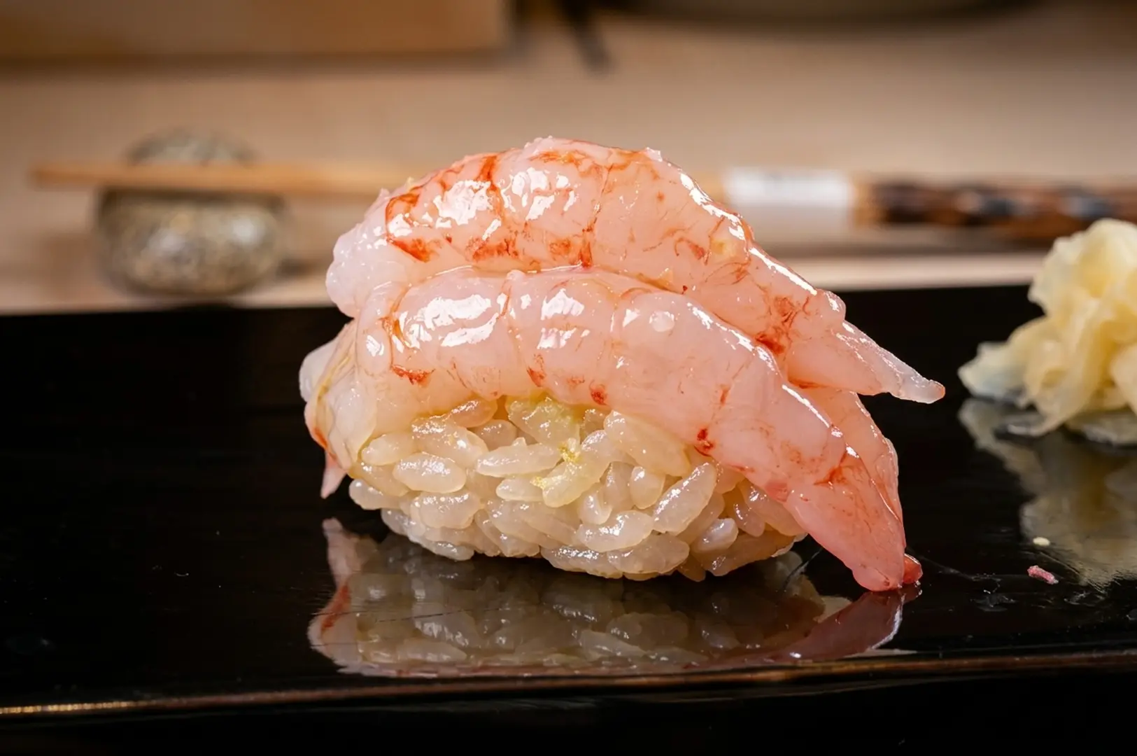 Close-up shot of glistening ebi (sweet shrimp) nigiri served on a black plate