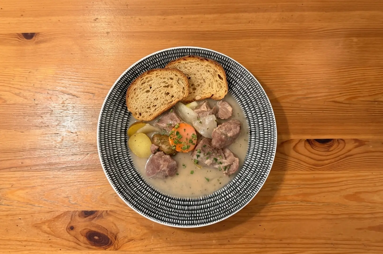 Rustic meat stew with vegetables and artisan bread served in decorative bowl on wooden table