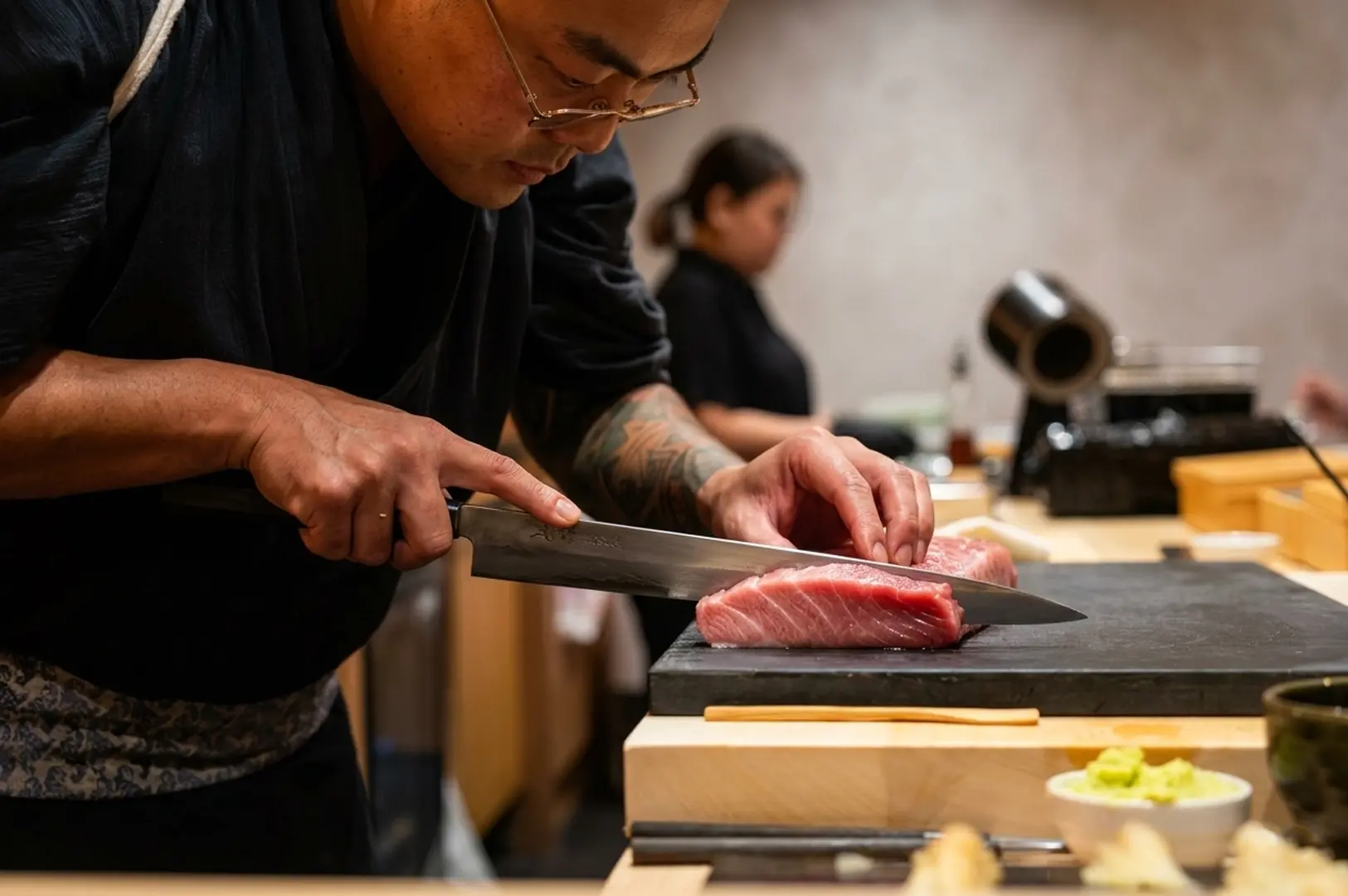 Chef carefully slicing fresh tuna with a long knife behind the counter at Sushi Masa