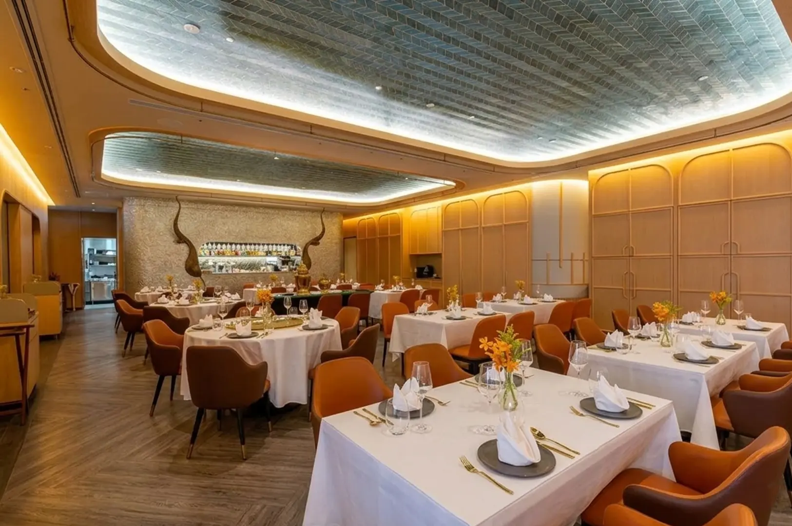 Elegant Thai or Vietnamese restaurant interior with white tablecloths, warm orange chairs, decorative ceiling, and ambient lighting