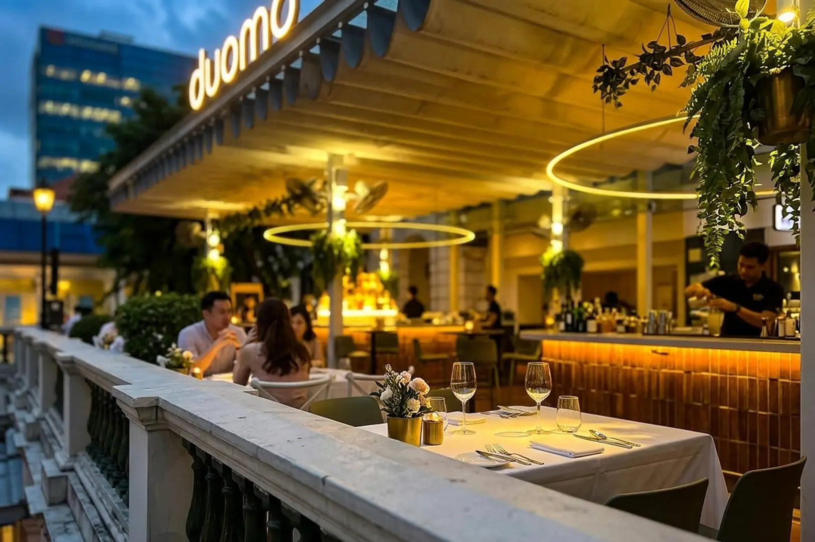 Duomo Italian restaurant exterior at twilight featuring al fresco dining tables with white linens, warm circular lighting, and patrons enjoying a relaxed romantic meal