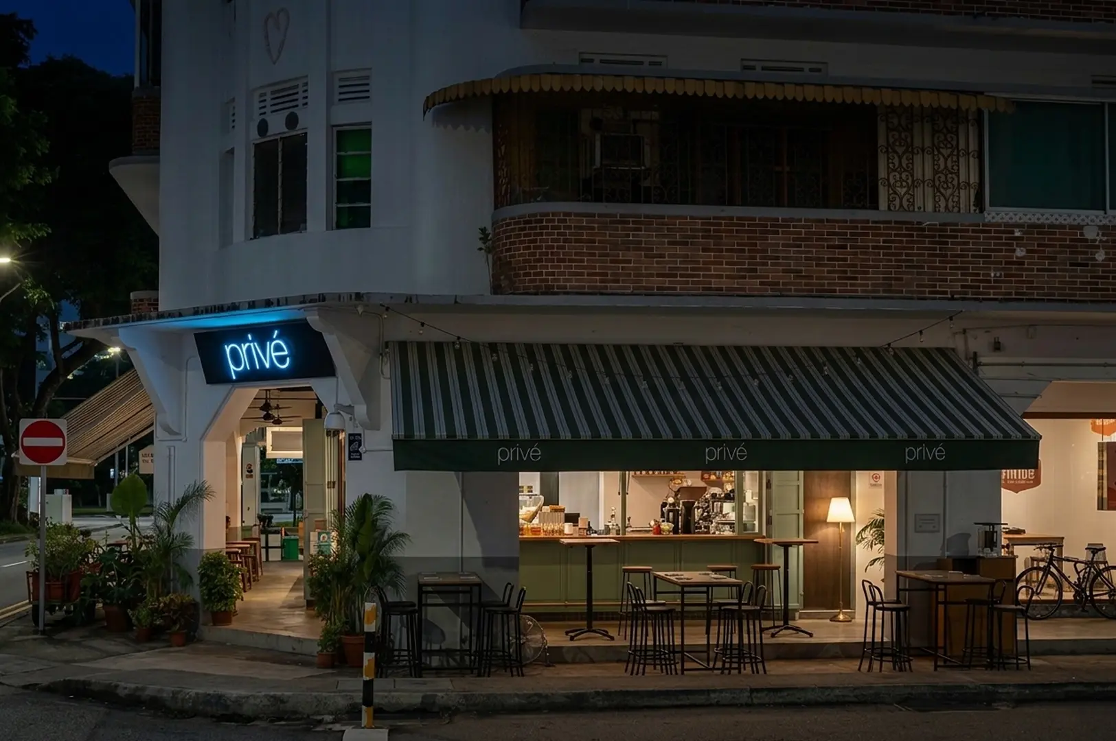 Night view of Privé cafe and bar located in a heritage corner shophouse in Joo Chiat, featuring a green striped awning and quiet outdoor seating